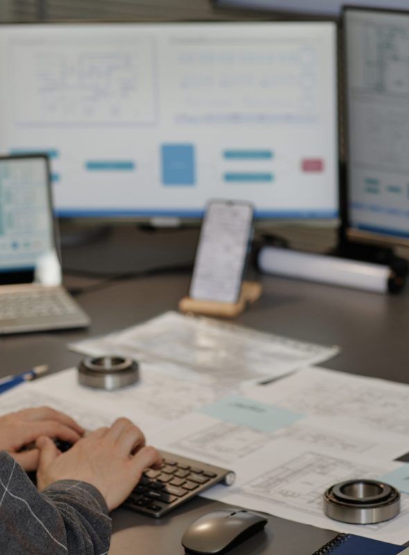Male engineer wearing hardhat n office and using computer designing blueprints